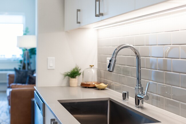 Kitchen with grey quartz countertops, white cabinetry, and grey subway tile backsplash - Avalon Bothell Commons