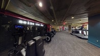 This fitness center combines an industrial aesthetic with a vibrant, energizing atmosphere designed to motivate members at every turn. The space features exposed concrete ceilings with gold-painted utility pipes running overhead, creating a raw, urban look that is complemented by bold accent walls in deep teal, crimson red, and warm yellow.

The cardio zone is anchored by a row of Life Fitness treadmills and elliptical trainers, set against a dark tiled accent wall adorned with a glowing neon "Seize the Day" sign — a standout motivational centerpiece. Adjacent to this area, a dedicated strength training section houses a variety of selectorized weight machines, a cable cross machine, and free weight benches, offering a comprehensive range of resistance training options. A BOSU ball and other functional training accessories are also available throughout the space.

Large mirrored panels line portions of the walls, visually expanding the space and assisting members with form and technique. A functional training area with stability balls, dumbbells, and plyometric boxes occupies a distinct zone, supported by built-in shelving for convenient equipment storage. Textured, dark carpet tiles cover the floors throughout, providing both comfort underfoot and a cohesive, polished finish. The overall ambiance is energetic and purposeful, making this a fully capable facility for a well-rounded workout.