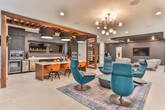 Located in Atlanta, GA, this sophisticated single-floor amenity space delivers a refined blend of modern design and versatile functionality. The layout flows seamlessly across several distinct zones, each thoughtfully appointed with contemporary furnishings and bold design choices.

The kitchen and dining area is a standout feature, boasting dark cabinetry, stainless steel appliances including a wall oven and beverage cooler, a sleek white-topped island with warm wood paneling, and dramatic drum pendant lighting with warm interior tones. A wall-mounted TV adds a media element to the culinary space.

The main lounge area commands attention with a coffered ceiling detail finished in deep charcoal, a textured accent wall, and a centrally positioned circular seating platform anchored by a cylindrical column — creating an inviting social hub. Swivel lounge chairs and curated artwork complete the upscale aesthetic.

The game room offers light hardwood flooring, a billiard table, ping-pong table, wall-mounted televisions, and seating nooks ideal for casual gatherings. Adjacent lounge areas feature leather and upholstered seating arrangements under stylish pendant and recessed lighting.

Additional spaces include a bright co-working nook with counter seating, large windows drawing in natural light, and transitional areas decorated with bold artwork and eclectic furnishings, reinforcing the space's dynamic, urban character throughout.