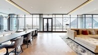Located at 250 Martin Luther King Jr Dr SW in the heart of Atlanta, Georgia, this upscale single-floor space offers a refined and versatile environment ideal for events, gatherings, or professional use. The open layout spans a generous footprint, designed to accommodate a variety of configurations with ease.

The space is defined by dramatic floor-to-ceiling glass curtain walls and dark-framed double doors that flood the interior with natural light while offering sweeping, unobstructed views of Mercedes-Benz Stadium and the surrounding Atlanta skyline. The herringbone-patterned hardwood flooring runs throughout, lending warmth and a sense of continuity to the open plan.

Distinct functional zones are thoughtfully arranged across the space. A long dining or work table with upholstered chairs anchors one side, while a lounge area features plush seating — including a tufted sofa, bold orange velvet accent chairs, and a round coffee table — arranged to encourage conversation. A built-in nook with teal curtained walls and marble-clad accent panels adds an architectural focal point, complemented by wall-mounted displays and soft ambient lighting.

Additional seating areas near the glass perimeter take full advantage of the panoramic outdoor views. The overall ambiance is modern and polished, blending premium materials, curated design details, and an abundance of natural light into a highly functional and visually striking space.