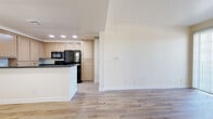 Located at 465 E Center St in Anaheim, California, this single-floor, 2-bedroom, 2-bathroom residence offers a clean, modern aesthetic with a practical and cohesive layout. Light wood-style flooring flows seamlessly throughout the entire unit, creating a bright and airy atmosphere across every room.

The open-concept kitchen and living area serves as the heart of the home. The kitchen features warm, light-toned cabinetry, dark granite countertops, recessed lighting, and a peninsula that provides additional prep space and separates it from the living area. Black appliances, including a refrigerator, microwave, and range, add a bold contrast to the cabinetry.

The living room receives generous natural light through multiple windows fitted with horizontal blinds, and a glass-paned exterior door provides direct outdoor access. The two bedrooms are well-sized, bright, and quiet, each with windows that bring in natural light and views of the surrounding greenery.

Both bathrooms are finished consistently, featuring warm wood-toned vanity cabinetry, white countertops, large mirrors, and light flooring. One bathroom includes a full shower-tub combination, while the other functions as a half bath. A dedicated closet adds valuable storage. The overall design is clean, neutral, and move-in ready.