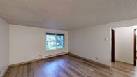 Located at 2632 E 27th Ave in Spokane, Washington, this one-bedroom, one-bathroom unit offers a compact and efficiently designed single-floor layout. Hardwood-style flooring runs throughout the living spaces, adding a clean, consistent look to the interior. The living room is bright and open, featuring a window that lets in natural light and offers a view of the surrounding greenery outdoors. Baseboard heating units are present in the living room and bedroom, ensuring comfortable warmth throughout the colder months. The textured ceilings are a consistent feature across the main rooms. The bedroom is a well-proportioned private retreat, also equipped with baseboard heating and a window that brings in natural light. Three closets provide generous storage relative to the unit's size. The kitchen includes wood-toned cabinetry, a white range, refrigerator, and a functional countertop workspace. The bathroom is straightforward and practical, featuring a vanity with a single sink, a wall mirror, a toilet, and a shower-tub combination. The overall layout is sensible and well-organized, making efficient use of the available space throughout.
