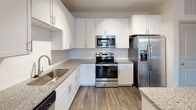 This single-story home in Charlotte, NC offers a clean, modern interior with thoughtfully selected finishes throughout. The open-concept living and dining area features rich wood-look flooring, crisp white walls, and a front entry door with transom window that invites natural light into the space. A sliding glass door provides direct outdoor access, further brightening the main living area.

The kitchen is well-appointed with white shaker-style cabinetry extending to the ceiling, granite countertops, a tile backsplash, and a full suite of stainless steel appliances including a French door refrigerator with ice and water dispenser, electric range, over-the-range microwave, and dishwasher. A central island with matching granite provides additional prep and counter space.

The bedroom features plush carpeting and a large window fitted with blinds, offering both comfort and natural light. The en-suite bathroom continues the granite countertop and white cabinetry theme, complemented by wood-look flooring, a glass-enclosed shower, and direct access to a spacious walk-in closet outfitted with wire shelving and hanging rods. The walk-in closet provides generous storage capacity to accommodate a variety of organizational needs.