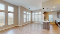 This single-floor residence showcases a thoughtfully designed open-concept layout that seamlessly connects the living and kitchen areas. The expansive living space is bathed in natural light, courtesy of a striking bank of floor-to-ceiling windows that line two walls, creating an airy and welcoming atmosphere. Light hardwood-style flooring runs throughout the main areas, complementing the warm, neutral-toned walls.

The kitchen is a standout feature, offering a galley-style configuration with a large peninsula island topped with white quartz countertops. Wood-grain cabinetry extends to the ceiling for generous storage, while stainless steel appliances — including a refrigerator, electric range, and built-in microwave — deliver a polished, modern aesthetic. Globe pendant lights add an elegant finishing touch above the island.

The bedroom features plush carpeting, a ceiling fan, and a window that invites natural light. An additional versatile room with hardwood-style flooring offers flexible use. Two bathrooms are finished with wood-grain vanities, white quartz countertops, and matte black hardware. The primary bathroom includes a walk-in shower with a glass enclosure, while the secondary bathroom features a tub-shower combo. An exterior door in the living area provides convenient outdoor access, rounding out this well-appointed space.