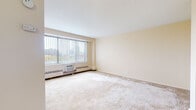 Located at 600 Asylum in Hartford, Connecticut, this single-floor unit offers a practical and well-organized layout suited for everyday living. The main living area is generously sized, finished with wall-to-wall carpeting and neutral, warm-toned walls that create a clean and inviting atmosphere. A large window dressed with vertical blinds allows abundant natural light to fill the space while providing views of the surrounding Hartford cityscape and treetops. A built-in wall unit air conditioner and baseboard heating ensure year-round comfort. The layout flows seamlessly into a secondary area with carpeted flooring and access to the unit's entry door, providing a natural transition between spaces. The kitchen is efficiently designed, featuring warm wood cabinetry, dark speckled countertops, a stainless steel sink, and a white gas range with overhead ventilation — offering all the essentials within a compact footprint. The bathroom is finished with classic white wall tiles accented by a teal border stripe, complementing a full soaking tub with chrome fixtures and a pedestal-style sink. Throughout the unit, the neutral color palette and straightforward design provide a functional and easy-to-personalize living environment in the heart of Hartford.