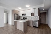 Located on the 23rd floor at 49 Walnut St S in downtown Hamilton, Ontario, this modern two-bedroom, two-bathroom unit offers an efficient and well-appointed layout with contemporary finishes throughout. Light wood-tone laminate flooring runs seamlessly across the open-plan living area, creating a bright and cohesive aesthetic.

The kitchen is a standout feature, equipped with stainless steel appliances including a refrigerator, electric range, and built-in microwave. White upper cabinetry pairs with warm wood-toned lower cabinets, complemented by a subway tile backsplash and a central island with a clean white countertop — ideal for both meal prep and casual dining.

Large floor-to-ceiling windows and a sliding glass door in the main living area fill the space with natural light and provide sweeping elevated views of the Hamilton cityscape and surrounding neighbourhoods. Both bedrooms are bright and functional, with the second bedroom featuring access to a private balcony.

The two bathrooms are finished in a clean, modern style. One features a glass-enclosed walk-in shower with wood-toned vanity cabinetry, while the other includes a full soaker tub with white tile surround and polished chrome fixtures. A hallway connects all rooms, adding to the practical flow of the unit.