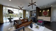 Located at 720 Michigan Ave in Columbus, Ohio, this single-floor communal space offers a thoughtfully designed environment that blends modern aesthetics with functional comfort. The open-plan layout centers around a stylish lounge area anchored by a rich cognac leather sofa and a plush tufted armchair, arranged around a sleek marble-topped coffee table. Two striking sputnik-style chandeliers serve as dramatic focal points overhead, casting warm ambient light across the space and complementing the recessed lighting throughout.

Floor-to-ceiling windows along one wall flood the interior with abundant natural light while framing lush outdoor views of landscaped greenery and a fenced terrace area, creating a seamless indoor-outdoor connection. Gold-toned drapery adds warmth and texture to the bright, airy atmosphere.

A built-in kitchenette is neatly integrated into a dark wood cabinetry wall, complete with appliances and shelving — ideal for casual entertaining or everyday convenience. An adjacent dining area with round tables and modern seating provides a setting for gathering and conversation.

The overall ambiance is contemporary and curated, with layered lighting, bold decorative accents, and a sophisticated mix of materials that create an inviting and dynamic communal environment.