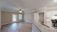 Located at 11010 Eastlake Club Dr in Raleigh, NC, this single-floor residence offers a well-designed open layout that seamlessly connects the kitchen, dining, and living areas. The kitchen is a standout feature, showcasing white shaker-style cabinetry, a subway tile backsplash, granite countertops, stainless steel appliances including a refrigerator and range, and a peninsula with an undermount sink — ideal for both cooking and casual dining. Light wood-style flooring flows throughout the main living areas, complementing the neutral gray walls and crisp white trim. Crown molding adds a refined architectural touch, while ceiling fans with light fixtures are present throughout, contributing to both comfort and style. The living area is bright and airy, benefiting from multiple windows and a glass-paneled exterior door that invites natural light. The bedrooms feature plush carpeting, ceiling fans, and natural light through slatted blinds, offering a cozy retreat. The bathroom is well-appointed with a white vanity, single-sink setup, a large mirror with elegant lighting, and a shower-tub combination. An open shelving nook and convenient in-unit laundry access add to the overall functionality of this comfortable Raleigh residence.