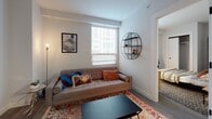 This single-floor residence at 50 Lecount Place in New Rochelle, New York, presents a thoughtfully designed layout with modern finishes and a clean, contemporary aesthetic. The living area features light wood-tone flooring, neutral walls, and a bright window that allows natural light to fill the space, creating a welcoming atmosphere. A circular wall-mounted shelf and framed artwork add character to the room.

The kitchen is outfitted with sleek gray cabinetry, stainless steel appliances including a range, dishwasher, and refrigerator, along with light countertops and under-cabinet lighting. A dining area adjacent to the kitchen comfortably accommodates a small table and chairs, making it practical for everyday living.

The bedroom offers a functional layout with sliding closet doors providing ample storage, light-toned flooring, and a window that brings in natural light. An open-frame metal shelving unit adds an industrial design element to the space.

The bathroom features marble-look tile flooring, a gray vanity with a white countertop, a large mirror with overhead lighting, and clean white walls, delivering a polished, modern finish throughout. Overall, the residence combines practical functionality with a cohesive contemporary design.