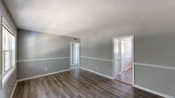 Located at 3151 Harris Dr in East Point, GA, this single-floor, one-bedroom, one-bathroom home offers a well-organized and functional layout. The interior is finished with durable hardwood-style flooring and a consistent cool gray color palette, accented by crisp white trim and chair rail molding that runs throughout the main living areas, lending a clean and cohesive aesthetic.

The living room is a generous, open space filled with natural light from a large multi-pane window. A front entry door provides direct access, and the room flows easily into the rest of the home via a connecting hallway.

The kitchen is well-appointed with white cabinetry extending to the ceiling for ample storage, granite-look countertops, and a full suite of stainless steel appliances including a refrigerator, range, and over-the-range microwave. A secondary exterior door and window in the kitchen area bring in additional natural light.

The bedroom is a comfortable, well-proportioned room featuring a ceiling fan, a natural light-filled window with an outdoor view, and a set of bifold closet doors providing convenient storage. The bathroom includes a full tiled tub-and-shower combination with classic white tile surround. A hallway connects all areas of the home, completing this practical and neatly finished single-story residence.