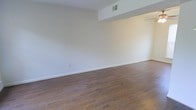 This two-story space showcases a straightforward, functional design characterized by clean lines and a neutral color palette. The main living area is finished with warm-toned hardwood flooring that extends throughout, providing a grounding contrast to the bright white walls and white baseboards. The open layout creates a spacious, airy feel, well-suited for a variety of furniture arrangements and uses.

A structural soffit detail near the ceiling adds subtle architectural interest, while a ceiling-mounted HVAC vent ensures climate control is seamlessly integrated into the design. The white walls are smooth and unadorned, offering a blank canvas for personalization. Electrical outlets are positioned at standard intervals along the walls, adding to the practicality of the space.

The overall ambiance is calm and understated, with the light-toned walls and natural wood flooring contributing to a bright, welcoming atmosphere. The two-floor configuration suggests additional living or functional space beyond what is immediately visible, expanding the overall versatility of the property.