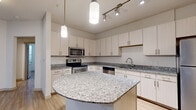 This well-appointed 4-bedroom, 2-bathroom single-story home offers a thoughtfully designed layout with a welcoming and functional flow throughout. The kitchen serves as a standout feature, showcasing a large granite-topped island with a curved edge, light wood cabinetry with sleek bar-pull hardware, and a full suite of stainless steel appliances including an electric range, over-the-range microwave, and dishwasher. A combination of pendant lighting and a track lighting system illuminates the space, complementing the light wood-style flooring that extends throughout the home. The living area is bright and open, benefiting from natural light through windows and a glass door that leads to the outdoors, complete with a ceiling fan overhead. The primary bedroom is generously sized, featuring wood-style flooring, a ceiling fan, and direct access to a private bathroom. Additional bedrooms offer closet access and open connectivity to the hallways. The bathrooms are finished with large-format tile flooring and include a shower-tub combo. A dedicated laundry area houses a stacked washer and dryer unit. With three closets and two hallways providing efficient circulation, this home balances practicality with comfortable, modern living.