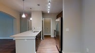 Located at 650 Enterprise Blvd in Charleston, South Carolina, this single-floor residence offers a clean, contemporary design with thoughtful finishes throughout. The kitchen serves as a central highlight of the space, showcasing a long galley-style layout with dark wood cabinetry that contrasts beautifully against crisp white quartz countertops. A deep undermount sink is elegantly illuminated by pendant lights, while a track lighting system runs the length of the ceiling, providing ample task lighting. Stainless steel appliances, including a French door refrigerator and oven range, lend a polished, modern aesthetic. The warm-toned luxury vinyl plank flooring flows seamlessly throughout, adding both durability and visual continuity across the space. Neutral wall tones in soft beige create a calm, welcoming ambiance that complements the modern fixtures. The layout offers an efficient, open corridor design that connects the kitchen to additional rooms beyond, suggesting a well-organized and functional floor plan. Natural light and recessed ventilation are integrated into the ceiling design, enhancing the overall comfort and livability of the space. This unit presents a well-appointed interior suited for modern living in the Charleston area.