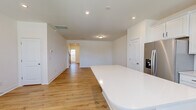 This two-story home is thoughtfully laid out across two well-proportioned floors of nearly equal size, offering a comfortable and functional living environment. The main floor features an open-concept kitchen and living area anchored by light hardwood-style flooring that runs throughout. The kitchen is equipped with stainless steel appliances, including a French door refrigerator with ice dispenser, a gas range, and a built-in microwave, all complemented by white cabinetry and a white quartz island. Natural light enters through multiple windows near the front entry, brightening the space. A conveniently located half bathroom on the main floor features a pedestal sink, round mirror, and wood-look tile flooring. A staircase with wood balusters connects to the upper level, where plush carpet extends through the hallways and all three bedrooms. The generously sized primary bedroom includes direct access to both a private bathroom and a dedicated walk-in closet outfitted with wire shelving systems. Additional bedrooms are well-sized and share access to the remaining bathrooms. A utility room and attached garage with an automatic opener complete the home's practical amenities.