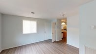 Located at 2110 Smallwood Dr in Wilson, NC, this single-story home offers a clean, well-maintained interior with a practical and open layout. Throughout the main living areas, light gray wood-look flooring creates a cohesive and easy-to-maintain foundation, complemented by soft blue-gray walls that lend a calm, neutral ambiance to the space.

The living area is open and airy, benefiting from a bright window fitted with blinds that allows natural light to filter in. A pendant light fixture marks the transition toward the kitchen, providing a subtle architectural detail that connects the two spaces visually.

The galley-style kitchen is efficiently designed, featuring warm wood cabinetry, a countertop with an integrated sink, a white electric range, and a full-size refrigerator. A mosaic tile backsplash adds a decorative touch, while track lighting overhead ensures the workspace is well-lit. The kitchen also provides access to an exterior door.

The bathroom includes a full tub and shower combo with white tile surround and chrome fixtures, offering a clean and functional design. A dedicated utility closet houses the water heater and includes overhead shelving, keeping mechanical systems neatly tucked away. Additional interior doors provide access to closet storage throughout the home, maximizing organizational functionality within the single-floor footprint.