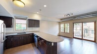 Located at 468 Delaware Ave in Buffalo, NY, this one-bedroom, one-bathroom unit offers a well-designed layout across a single floor. A welcoming hallway with rich hardwood flooring and recessed lighting leads into the main living area. The open-concept kitchen and living room serve as the heart of the unit, featuring dark espresso cabinetry, granite countertops, a curved breakfast bar island, and stainless steel appliances. Large windows bathe the space in natural light, while a sliding glass door opens onto a private balcony with outdoor views — ideal for enjoying the surrounding neighborhood. Exposed ductwork adds an industrial loft-inspired character to the living area, complemented by track lighting overhead. The bedroom is carpeted with patterned blue flooring, includes a closet with louvered doors, and benefits from a generous window that invites additional natural light. The bathroom is appointed with large-format dark tile flooring and wall tile in the walk-in shower area, a dark wood vanity with granite countertop, and a clean, modern aesthetic. A dedicated closet and hallway complete this thoughtfully arranged unit, offering practical storage and a cohesive design throughout.