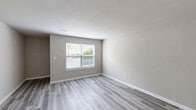 Located at 6 S Kingsbridge Pl in Chesapeake, VA, this single-floor, one-bedroom, one-bathroom home offers a well-designed layout with modern finishes throughout. Light gray luxury vinyl plank flooring runs consistently across the entire space, complementing the neutral, warm-toned walls and crisp white trim found in every room.

The living room is a bright, open area with natural light filtering through a window fitted with blinds. It flows naturally into the rest of the home via a connecting hallway. The kitchen is a functional galley-style space featuring white shaker-style cabinetry, granite countertops with flecked detailing, a double stainless steel sink, and a stainless steel range, offering efficient and attractive workspace.

The bedroom is a comfortable, well-proportioned room with a window that brings in natural light and views of the surrounding greenery. The room connects to a hallway that provides access to the full bathroom, which includes a soaking tub and shower combination with clean white tile surround and brushed gold fixtures. Two closets offer generous storage options throughout the unit.

A dedicated laundry area with washer/dryer hookups, a utility shelf, and a floor drain adds practical convenience. The overall design is clean, cohesive, and move-in ready.