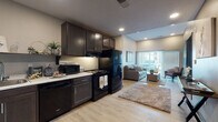 Located on E Cherry Street in Springfield, Missouri, this single-floor residential unit offers a well-organized layout designed with both functionality and modern aesthetics in mind. The open-concept kitchen flows directly into the living area, creating a cohesive and efficient use of space. The kitchen is equipped with dark espresso cabinetry, light marble-style countertops, black appliances including a refrigerator, range, dishwasher, and microwave, and an open display shelf. Light wood-style flooring runs throughout the main living areas, contributing to a clean, contemporary feel.

The living room receives generous natural light through large sliding glass doors fitted with sheer vertical blinds, offering outdoor views and a bright, airy atmosphere. A dedicated flex room with carpeted flooring provides additional versatility, suitable for use as a dining area or office. The bedroom features plush carpet, a ceiling fan, and a window for natural light.

Two bathrooms are present, each finished with geometric marble-style tile flooring and dark vanity cabinetry. One bathroom includes accessibility features such as grab bars near the toilet and tub. A walk-in closet is accessible from one of the bathrooms, adding practical storage. The unit's entry features a bold dark-painted steel door, reinforcing its modern character.