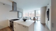 Located in Chicago's vibrant River North neighborhood, this single-floor unit at 711 N State St offers a sleek, contemporary design with an emphasis on natural light and open living. Floor-to-ceiling windows span the living and dining areas, framing dynamic city views of the surrounding skyline and streetscape, while flooding the interior with abundant daylight.

The open-plan layout connects the kitchen, dining, and living areas seamlessly. The kitchen is outfitted with white flat-front cabinetry, stainless steel appliances, a gas cooktop, a stainless range hood, and a generous white quartz island with bar seating—ideal for both casual dining and entertaining. The living area accommodates a comfortable seating arrangement, complemented by curated artwork and a refined neutral palette.

The bedrooms continue the modern aesthetic, each featuring large windows with urban views, soft carpeting, and clean-lined furnishings. The bathrooms are finished with light wood-tone tile flooring, white vanities with undermount sinks, large mirrors, and glass-enclosed showers, maintaining a consistent minimalist sensibility throughout. Overall, the space presents a polished, contemporary environment well-suited to urban living.