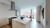 Located in Chicago's vibrant River North neighborhood, this single-floor unit at 711 N State St offers a sleek, contemporary design with an emphasis on natural light and open living. Floor-to-ceiling windows span the living and dining areas, framing dynamic city views of the surrounding skyline and streetscape, while flooding the interior with abundant daylight.

The open-plan layout connects the kitchen, dining, and living areas seamlessly. The kitchen is outfitted with white flat-front cabinetry, stainless steel appliances, a gas cooktop, a stainless range hood, and a generous white quartz island with bar seating—ideal for both casual dining and entertaining. The living area accommodates a comfortable seating arrangement, complemented by curated artwork and a refined neutral palette.

The bedrooms continue the modern aesthetic, each featuring large windows with urban views, soft carpeting, and clean-lined furnishings. The bathrooms are finished with light wood-tone tile flooring, white vanities with undermount sinks, large mirrors, and glass-enclosed showers, maintaining a consistent minimalist sensibility throughout. Overall, the space presents a polished, contemporary environment well-suited to urban living.