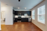 This single-floor unit showcases a thoughtfully designed interior that blends modern aesthetics with practical functionality. The kitchen serves as a central highlight, featuring floor-to-ceiling dark navy shaker-style cabinetry with gold hardware, granite countertops, and a striking herringbone-patterned tile backsplash. A full suite of stainless steel appliances—including a bottom-freezer refrigerator, electric range, over-the-range microwave, and dishwasher—completes the space, alongside a gold-finish undermount sink.

Warm hardwood-style flooring runs consistently throughout the unit, creating visual continuity between the open kitchen and living areas. The living space benefits from multiple windows fitted with white blinds, allowing ample natural light, while a sleek ceiling fan with integrated lighting adds comfort and style.

The hallway features a distinctive design detail: white barn-style sliding doors with matte black hardware, adding a contemporary architectural touch. Bedrooms are well-proportioned and bright, with additional windows and ceiling fans providing ventilation and outdoor views.

The bathroom is cleanly finished with large-format beige wall tiles surrounding a soaking tub and shower combination, accented by brushed gold fixtures and a matte black curved curtain rod, maintaining the unit's cohesive mixed-metal design theme.