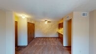 This single-floor residential unit offers a practical and comfortable layout designed for everyday living. The open living and dining area is finished with wall-to-wall carpet and features a ceiling fan with light fixture, a closet with warm-toned wood panel doors, and a pass-through connection to the kitchen. Natural light fills the main living space through a sliding glass door fitted with vertical blinds, offering a view of the outdoors. The spacious bedroom is carpeted and receives natural light through a window with blinds, providing a quiet and restful environment. The galley-style kitchen is efficiently laid out with warm wood cabinetry lining both sides, a double stainless steel sink with white countertops, black appliances including a range, microwave, and refrigerator, and durable tile flooring. The bathroom features the same tile flooring as the kitchen, a full bathtub and shower combination with chrome fixtures and grab bars, and a standard toilet. Throughout the unit, textured ceilings add a classic residential character, while the neutral wall tones and consistent finishes create a cohesive and livable atmosphere. The entryway features tile flooring and an adjacent closet, providing a well-defined transition into the main living area.