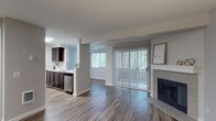 This single-story residence is thoughtfully designed with an open-concept layout that promotes a seamless flow between living spaces. Wood-style flooring runs throughout the main living and kitchen areas, adding warmth and visual continuity, while soft, neutral-toned walls create a clean and welcoming atmosphere.

The living area serves as the central gathering space, anchored by a classic fireplace with a white mantle and tile surround. A large sliding glass door fitted with vertical blinds fills the room with natural light and provides access to an outdoor area, with views of greenery visible through adjacent windows. A ceiling fan is installed in the adjoining area, enhancing airflow and comfort.

The galley-style kitchen is well-appointed with rich dark cabinetry, white countertops, a stainless steel sink, and stainless steel appliances including a refrigerator and dishwasher. A tiled backsplash adds a refined finishing touch.

A separate bedroom features plush carpeting, a window for natural light, and a pass-through window connecting to an adjacent area. The bathroom is outfitted with a dark wood vanity, a single-sink countertop, a wall mirror, and a full bathtub with shower, all set on wood-style flooring for a cohesive aesthetic.