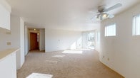 This single-floor residence showcases a thoughtfully designed open layout that connects the living and dining areas to the kitchen seamlessly. The spacious living area features a gently curved wall design, soft neutral carpeting, and a ceiling fan with integrated lighting. Large sliding glass doors open directly onto a private balcony, which is accompanied by multiple windows offering views of surrounding treetops, filling the space with generous natural light throughout the day.

The kitchen is positioned at the heart of the unit, defined by a peninsula counter that separates it from the main living space. It includes white cabinetry, light countertops, tile flooring, and white appliances including a coil-burner electric range and full-size refrigerator, alongside an overhead range hood.

The bedrooms are carpeted and well-proportioned, each offering ample wall space. One bedroom includes a sliding-door closet and an electrical panel, while another features a baseboard heater and a window with blinds for light control.

The bathroom presents a dual-sink vanity with light countertops, tile flooring, and mirrored medicine cabinets above, offering practical functionality. Overall, the unit maintains a clean, neutral palette throughout.