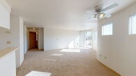 This single-floor residence showcases a thoughtfully designed open layout that connects the living and dining areas to the kitchen seamlessly. The spacious living area features a gently curved wall design, soft neutral carpeting, and a ceiling fan with integrated lighting. Large sliding glass doors open directly onto a private balcony, which is accompanied by multiple windows offering views of surrounding treetops, filling the space with generous natural light throughout the day.

The kitchen is positioned at the heart of the unit, defined by a peninsula counter that separates it from the main living space. It includes white cabinetry, light countertops, tile flooring, and white appliances including a coil-burner electric range and full-size refrigerator, alongside an overhead range hood.

The bedrooms are carpeted and well-proportioned, each offering ample wall space. One bedroom includes a sliding-door closet and an electrical panel, while another features a baseboard heater and a window with blinds for light control.

The bathroom presents a dual-sink vanity with light countertops, tile flooring, and mirrored medicine cabinets above, offering practical functionality. Overall, the unit maintains a clean, neutral palette throughout.