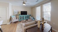 This single-floor residence offers a thoughtfully designed open-concept layout with warm wood-look flooring and crown molding throughout the main living areas. The living room is bright and welcoming, featuring a ceiling fan, large windows, and a glass-paned door that opens to a private balcony, flooding the space with natural light. A teal accent wall adds a pop of coastal-inspired color that ties seamlessly into the décor.

The kitchen is a standout feature, showcasing rich dark cabinetry, granite countertops, and a full suite of stainless steel appliances. A peninsula with pendant lighting and bar seating creates an ideal space for casual dining and entertaining. A dedicated dining area adjacent to the kitchen completes the open living and dining arrangement.

The bedroom is generously sized with plush carpeting, a ceiling fan, and a bold blue accent wall that lends a calm, restful atmosphere. Natural light filters through large windows offering views of the surrounding neighborhood.

The bathroom is well-equipped with a wide granite-topped vanity, dark wood cabinetry with ample storage, and a large mirror with overhead lighting. A dedicated laundry room with a full-size washer and dryer and overhead shelving adds everyday convenience to this functional and stylish residence.