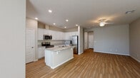 This two-story home is thoughtfully designed with a clean, modern aesthetic and a neutral color palette throughout. The main level centers around an open-concept kitchen and living area, where wood-look tile flooring flows seamlessly underfoot. The kitchen is well-appointed with crisp white cabinetry, granite countertops, a stainless steel appliance suite including a range, microwave, and refrigerator, and a central island with a built-in sink offering additional prep and seating space. Recessed lighting illuminates the area, while a ceiling fan in the adjacent living space adds comfort. A keypad-equipped entry door provides convenient access directly into this main living area.

The upper level hosts the bedrooms, each finished with plush carpeting, ceiling fans with light fixtures, and windows that bring in natural light. The primary suite includes a spacious walk-in closet with built-in shelving and hanging rods, as well as a private en-suite bathroom featuring a dual-sink vanity with granite countertops, white cabinetry, and a separate tub and shower combination. A secondary full bathroom mirrors the same refined finishes, with a granite-topped vanity and a tub-shower unit. The home's consistent use of granite surfaces and white cabinetry creates a cohesive and polished look throughout.