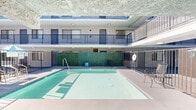 Located at 951 S Oxford Ave in the heart of Los Angeles, this property features a well-appointed central courtyard that serves as a communal hub for residents. The standout feature of this outdoor space is a generously sized swimming pool with clear, blue-green water, enclosed by a secure metal fence gate for safety. The pool is framed by a wide, open deck area that accommodates outdoor seating, including metal chairs and a small accent stool, making it an inviting space for relaxation and recreation. A lush, floor-to-ceiling green wall panel anchors one side of the courtyard, providing a vibrant natural aesthetic contrast to the building's neutral stucco exterior. The courtyard is embraced on multiple sides by the surrounding multi-story structure, whose upper levels feature walkways lined with dark metal railings that overlook the pool area below. Ceiling-mounted light fixtures are positioned along the covered corridors, ensuring the space is well-lit at all hours. An umbrella-shaded seating area near the pool entrance offers additional comfort for outdoor gatherings. The open-air design of the courtyard allows for abundant natural light to flood the space throughout the day, creating a bright and welcoming atmosphere in the midst of urban Los Angeles.