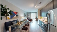 Located at 465 M St SW in Washington, DC's Southwest Waterfront neighborhood, this thoughtfully designed single-floor residence offers a seamless blend of modern aesthetics and functional living. The open-concept layout connects the kitchen, dining, and living areas, creating a bright and cohesive space bathed in natural light from large sliding glass doors that lead to outdoor views of lush greenery.

The kitchen is outfitted with dark wood cabinetry, white quartz countertops, a subway tile backsplash, and a full suite of stainless steel appliances, including a range, microwave, and refrigerator. Light wood-style flooring runs throughout the main living areas, enhancing the contemporary feel.

The living room offers generous space with neutral-toned walls and access to the outdoor balcony, while the adjacent dining area accommodates a full-sized table with ease. Two well-proportioned bedrooms each feature large windows that invite natural light and views of the surrounding greenery, along with ample closet space including mirrored sliding doors.

The unit includes two bathrooms: one with a walk-in glass shower and access to a walk-in closet, and a second with a tub-shower combination. Both feature dark wood floating vanities and large framed mirrors, maintaining a consistent, polished design throughout.