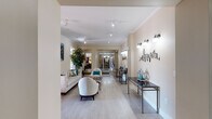 Located at 1901 N Lincoln Ave in Urbana, Illinois, this single-floor community amenity space offers a diverse range of thoughtfully designed areas for relaxation, entertainment, and wellness. The entrance welcomes visitors through glass-paneled doors into a bright, open corridor with light hardwood flooring and crown molding throughout.

The elegant lounge area features neutral-toned walls, modern track lighting, and stylishly curated furnishings including plush sofas, rounded accent chairs, and a zebra-print ottoman, all complemented by bold artwork and decorative wall accents. A dedicated theater room and a signposted corridor lead residents to additional amenities deeper within the space.

The game and social room contrasts the lounge with rich, dark hardwood floors, coffered ceilings, corrugated metal wainscoting, and large street-facing windows that fill the room with natural light. A billiard table, a lounge seating area with leather sectionals, and a kitchenette with full-size appliances make this a versatile gathering space.

The fitness center is well-equipped with cardio machines including treadmills and a stationary bike, along with strength training equipment, free weights, and a large wall mirror — all set on durable rubberized flooring. Together, these amenity spaces provide a comprehensive and polished communal environment.