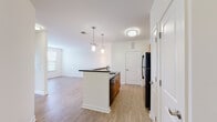 Located at 1010 Acropolis Way in Frederick, Maryland, this single-floor residence offers a clean, modern design highlighted by light wood-style flooring and a bright, neutral color palette that flows consistently throughout the space.

The kitchen serves as a central feature of the home, anchored by a substantial island with dark granite countertops and pendant lighting overhead. Warm-toned wood cabinetry extends to the upper walls, providing ample storage, while black appliances—including a refrigerator, electric range, and over-the-range microwave—offer a cohesive, contemporary aesthetic. The island configuration creates a natural transition into the open living area, which benefits from a large window that allows natural light and outdoor views to fill the room.

The bedroom is a well-proportioned space with the same light flooring, crisp white walls, and a double-door closet offering generous storage. The bathroom features wood-toned cabinetry with a vanity, a toilet, and clean, simple finishes consistent with the rest of the home. Throughout the residence, white paneled doors, visible ventilation, and clean baseboard trim contribute to a tidy, well-maintained overall ambiance.