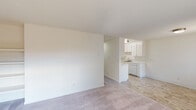 This single-floor residence offers a straightforward, functional layout with a bright and neutral aesthetic throughout. The open living area features plush carpeting that transitions to wood-look vinyl flooring, creating a clear distinction between living and kitchen zones. Large windows with vertical blinds allow natural light to fill the space, and a wall-mounted air conditioning unit ensures year-round comfort.

The galley-style kitchen is well-equipped with ample white cabinetry, light-toned countertops, a tile backsplash, and a full suite of white appliances including a range, microwave, refrigerator, and dishwasher. A stainless sink with a brushed gold faucet completes the efficient workspace.

The bedrooms are carpeted and generously proportioned, each featuring sliding-door closets with built-in hanging rods for organized storage. Windows provide natural light and views of the surrounding exterior. Baseboard heating units are present in the bedrooms for added warmth.

A hallway connects the living spaces to the bathroom, which includes a single-sink vanity with white cabinetry, a large mirror with contemporary light fixtures, and wood-look flooring. The overall design is clean and minimal, making the space highly adaptable to a variety of living arrangements.