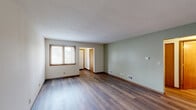 Located at 716-732 Sheridan Rd in Somers, Wisconsin, this 2-bedroom, 2-bathroom residence offers a well-organized single-floor layout designed for comfortable everyday living. The entrance opens into a spacious hallway that connects to the main living areas, all finished with warm wood-style flooring that runs throughout the common spaces. The open-concept living and dining area is bright and generously proportioned, with neutral walls in soft sage green and cream tones that create a calm, inviting atmosphere. A pass-through window connects the living area to the kitchen, which features warm oak cabinetry, dark granite-style countertops, and black appliances including a full-size refrigerator. The primary bedroom is notably spacious, also featuring wood-style flooring and a window that allows in natural light. The second bedroom is carpeted with a window offering views of surrounding greenery. Both bathrooms are well-appointed, with one featuring a full tub-shower combination, warm wood vanity, and a mirrored medicine cabinet. Additional practical features include three closets, a dedicated laundry room, an attached garage, and a patio. Lush tree coverage visible from the windows adds a pleasant natural backdrop to this functional and well-laid-out home.