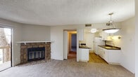 This single-floor residence offers a functional and comfortable layout with a warm, neutral aesthetic throughout. The living area is a standout space, anchored by a classic stone fireplace with brass-trimmed glass doors, creating a cozy focal point. Soft carpeting extends through the living and dining areas, while a sliding glass door opens to a private balcony with views of surrounding greenery, bringing in natural light and a pleasant outdoor connection.

The kitchen is well-appointed with white cabinetry, dark countertops, and wood-look flooring. It features full appliances including a refrigerator, electric range, and dishwasher, along with ample upper and lower cabinet storage and under-cabinet lighting. A peninsula separates the kitchen from the living space, and a pendant light illuminates the adjacent dining area.

The bedrooms are carpeted and bright, each featuring vertical blinds over windows that allow for natural light. The layout flows easily between rooms via a central hallway.

The bathroom includes a full tub-shower combination, a white vanity with sink, and built-in shelving for added storage. Wood-look flooring and a window above the tub provide both practicality and ventilation. Throughout the residence, a textured ceiling, neutral wall tones, and consistent finishes contribute to a cohesive and livable environment.