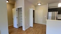 This single-floor residence offers a clean and functional layout with a warm, neutral aesthetic throughout. The entryway sets the tone with light-toned hardwood-style flooring that extends seamlessly across the space, creating a cohesive and inviting atmosphere. Soft beige walls complement the white trim and door frames, lending the interior a bright, well-maintained appearance.

A standout feature near the entry area is a built-in open shelving closet with multiple tiers, providing generous and accessible storage for everyday essentials. The closet is framed by classic paneled bifold doors, adding a traditional touch to the space. Adjacent to it, a secondary door leads to an additional room or storage area, contributing to the overall utility of the layout.

The main entrance door is solid and features a modern lever-style handle, offering both security and style. Overhead, a flush-mount ceiling light fixture provides practical illumination, while the visible HVAC vent suggests a centralized climate control system. The elevated wall height adds a sense of openness without feeling overwhelming. Overall, the space balances simplicity with functionality, making it a practical and comfortable environment well-suited for everyday living.