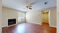 This single-story home offers a well-organized layout with a comfortable blend of functional spaces and practical finishes. The living room serves as the central gathering area, showcasing rich wood-look flooring, a classic fireplace framed by a clean white surround, and a ceiling fan overhead. A window brings in natural light and offers views of surrounding greenery, creating a warm and inviting atmosphere. The textured ceiling adds a traditional touch consistent throughout the home.

A hallway fitted with a smart thermostat connects the living area to the private quarters, leading to multiple bedrooms. Each bedroom features plush wall-to-wall carpeting, a ceiling fan with integrated lighting, and windows that invite natural light. The rooms offer a quiet, neutral palette suitable for various furnishing arrangements.

The galley-style kitchen is equipped with warm wood cabinetry, light countertops, and a full suite of white appliances including a refrigerator, range, microwave, and dishwasher, all set atop wood-look flooring. Two bathrooms feature tiled tub-shower combinations with chrome fixtures and wood-look flooring. A dedicated laundry area accommodates a full-size washer and dryer, adding everyday convenience to this practical, move-in-ready home.