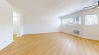 Located at 4143 Palmwood Dr in the heart of Los Angeles, CA, this one-bedroom, one-bathroom unit offers a clean, modern aesthetic across a single thoughtfully laid-out floor. Light wood-tone flooring flows consistently throughout the living areas and bedroom, creating a warm, cohesive feel. Bright white walls and natural light from multiple slatted-blind windows contribute to an open, airy atmosphere throughout the space.

The combined kitchen and living room area forms the heart of the unit. The kitchen features white cabinetry, light-toned countertops, a stainless steel double-basin sink, a stainless steel refrigerator, and a gas range, all complemented by tile flooring and windows that invite natural light. The adjacent living area offers generous open floor space with a wall-mounted A/C unit and outdoor views through wide windows.

The bedroom is a comfortable, well-lit retreat with two windows, a wall-unit A/C, a ceiling fan, and a mirrored sliding-door closet that enhances the sense of space. A hallway connects the bedroom to the full bathroom, which includes a tub/shower combo with tile surround, a toilet, tile flooring, and a window for natural ventilation. The layout is efficient and functional, making excellent use of the available space throughout.