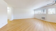Located at 4143 Palmwood Dr in the heart of Los Angeles, CA, this one-bedroom, one-bathroom unit offers a clean, modern aesthetic across a single thoughtfully laid-out floor. Light wood-tone flooring flows consistently throughout the living areas and bedroom, creating a warm, cohesive feel. Bright white walls and natural light from multiple slatted-blind windows contribute to an open, airy atmosphere throughout the space.

The combined kitchen and living room area forms the heart of the unit. The kitchen features white cabinetry, light-toned countertops, a stainless steel double-basin sink, a stainless steel refrigerator, and a gas range, all complemented by tile flooring and windows that invite natural light. The adjacent living area offers generous open floor space with a wall-mounted A/C unit and outdoor views through wide windows.

The bedroom is a comfortable, well-lit retreat with two windows, a wall-unit A/C, a ceiling fan, and a mirrored sliding-door closet that enhances the sense of space. A hallway connects the bedroom to the full bathroom, which includes a tub/shower combo with tile surround, a toilet, tile flooring, and a window for natural ventilation. The layout is efficient and functional, making excellent use of the available space throughout.