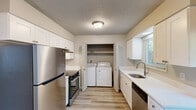 Located in Portland, Oregon, this two-story, 2-bedroom, 1-bathroom home offers a practical and well-organized layout spread across two floors. The main level features a bright, open living room with light hardwood-style flooring, a textured ceiling, vertical shiplap accent wall, and a large window that brings in natural light and views of the surrounding greenery. A carpeted staircase with a metal railing leads to the upper level. The combined dining and kitchen area is efficiently designed with white shaker-style cabinetry, stainless steel appliances including a refrigerator, gas range, and dishwasher, and a single-basin sink beneath a window. A dedicated in-unit laundry closet with a full-size washer and dryer is conveniently located within the kitchen. Upstairs, the spacious primary bedroom features a wide window with outdoor views, light flooring, and multiple closets. The second bedroom is well-sized and similarly finished. The full bathroom includes a tub-shower combo with large white tile surround, a vanity with white cabinetry, and a small privacy window. Throughout the home, consistent light-toned flooring, neutral walls, and textured ceilings create a clean and cohesive aesthetic.