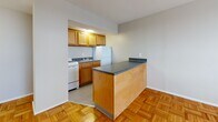 Located at 518 E Town St in Columbus, Ohio, this efficiently designed single-floor unit offers a well-organized layout that makes smart use of its compact footprint. The living area is bright and open, featuring classic parquet wood flooring that extends throughout the space, neutral gray walls, and a window fitted with an air conditioning unit to ensure year-round comfort.

The kitchen is thoughtfully separated from the living area by a peninsula-style breakfast bar with a dark granite-look countertop, providing both additional prep space and a natural visual divider. The kitchen itself is equipped with warm honey-toned wood cabinetry, a white range, a white refrigerator, and a sink, all set atop tile flooring.

Two closets offer practical storage solutions; one features a built-in vanity with a mirror, bench seating, a drawer, and a full-length clothing rod with hooks — a versatile and functional touch.

The bathroom is finished in a clean, all-white palette with tile flooring, a combination tub and shower, a pedestal sink, a toilet, and a window that allows for natural ventilation and light. The overall ambiance of the unit is clean, functional, and move-in ready, well-suited for those seeking a manageable, low-maintenance living space in the heart of Columbus.