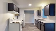 This single-floor unit offers a clean, functional layout with consistent laminate wood-style flooring running throughout the space, lending a cohesive and modern feel. The kitchen is efficiently designed with dark gray cabinetry, light countertops, a double stainless steel sink, and white appliances including a full-size refrigerator. Upper wall-mounted cabinets provide additional storage, and the space connects openly to the living and dining areas. The main living area is generously proportioned, featuring neutral gray walls, a textured ceiling, and a wall-mounted HVAC unit. An adjacent area with warm-toned flooring opens directly to the kitchen, offering versatile use as a dining or secondary living space. The bedrooms are bright and inviting, each benefiting from multiple windows with exterior views and baseboard heating. One bedroom features a ceiling fan and a built-in closet with shelving, while another includes a reach-in closet. An entry area provides a dedicated closet alongside a baseboard heater. The full bathroom is fitted with a tub-shower combination, accessibility grab bars, a white vanity with storage, and matching laminate flooring. Throughout, the unit maintains a neutral palette and a clean, move-in-ready presentation.