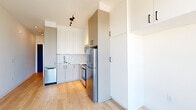 Located at 1922 NW Pettygrove St in Portland, Oregon, this efficiently designed single-floor unit offers a thoughtful layout that maximizes every square foot. The interior features light wood flooring throughout, crisp white walls, and matte black hardware accents that lend a cohesive, contemporary aesthetic.

The kitchen is well-appointed for its footprint, featuring an L-shaped layout with two-tone cabinetry — white upper cabinets and gray lower cabinets — complemented by a glossy white subway tile backsplash. Stainless steel appliances include a refrigerator, range with oven, over-the-range microwave, and dishwasher, making the space fully functional. Floor-to-ceiling cabinetry provides generous storage, and track lighting overhead keeps the area bright and practical.

The main living area is open and airy, anchored by a large picture window that frames elevated views of the surrounding Portland neighborhood, filling the space with natural light. A stacked washer and dryer unit is also included within the unit.

The bathroom maintains the clean, minimal style of the rest of the space, with a white vanity, matte black fixtures, and a walk-in shower with a black rail and wall-mounted hardware. Light wood flooring continues here, tying the unit together seamlessly.