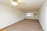 This single-floor residential unit offers a practical and well-organized layout designed for comfortable everyday living. The kitchen is efficiently arranged with white appliances, including an electric coil range, over-the-range microwave, and full-size refrigerator. Upper cabinetry with wood-trimmed doors provides ample storage, while a butcher block countertop adds a warm, functional touch. Light hardwood-style flooring runs through the kitchen area, transitioning seamlessly into the main living spaces.

The living and bedroom areas feature plush neutral carpet underfoot, creating a cozy atmosphere throughout. Each room is equipped with a ceiling fan with integrated light fixture, promoting air circulation and providing overhead lighting. Baseboard heating units ensure warmth during cooler months, and windows dressed with horizontal blinds allow for natural light and privacy control. The rooms are generously proportioned, offering flexible use of space.

The bathroom is clean and straightforward, featuring a full-size soaking tub with a shower rod and paneled surround, a toilet, and a vanity. Neutral tones throughout the unit lend a calm, cohesive aesthetic. The overall design is functional and practical, suited for a range of occupants seeking a move-in-ready single-level living space.