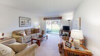 This efficient single-story home features three bedrooms and one bathroom within a well-organized floor plan. The living room serves as the central gathering space, finished with plush carpeting and a sliding glass door that fills the room with natural light and provides views of a lush green outdoor area. The kitchen is equipped with gray cabinetry, light granite-style countertops, tile flooring, and stainless steel appliances including a dishwasher and refrigerator. Adjacent to the kitchen, the dining area accommodates a four-seat table beneath a ceiling fan with built-in lighting, also finished with tile flooring for easy maintenance. The primary bedroom offers carpeted flooring, a closet, and windows that invite natural light, while the additional bedrooms are similarly appointed with carpet and windows. One bedroom features a dresser with built-in drawers beneath a window with decorative valance treatments, providing added storage. The shared full bathroom includes a tub-shower combination with brown tile surround, tile flooring, and a granite-topped vanity. Throughout the home, clean white walls and neutral finishes create a bright, cohesive aesthetic well-suited for comfortable everyday living.