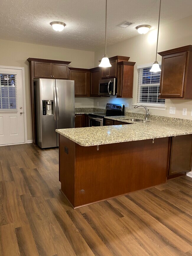 Cocina con encimeras de granito, gabinetes escalonados renovados, electrodomésticos de acero inoxidable y una península para sentarse en taburetes de bar. - 5497 Cedar Ash Crossing