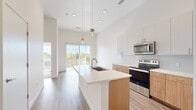 Located at 1298 Lamar St in Lakewood, Colorado, this thoughtfully designed one-bedroom, one-bathroom unit offers a clean, modern aesthetic throughout. Soaring ceilings in the open-concept living and kitchen area create an airy, expansive atmosphere, with recessed lighting and stylish pendant fixtures adding a contemporary touch. The kitchen is a standout feature, equipped with stainless steel appliances including a range, microwave, and refrigerator, complemented by warm wood-toned lower cabinetry, crisp white upper cabinets, and a subway tile backsplash. A central island with a quartz countertop and undermount sink provides both workspace and a natural gathering point. Wood-look flooring runs throughout the main living area, leading to a sliding glass door that opens to a private balcony with views of the surrounding greenery. The bedroom is a calm retreat featuring plush carpeting, high ceilings, and large windows that invite abundant natural light. The bathroom is finished with matching wood-toned cabinetry, a quartz vanity top, a glass-enclosed shower, and direct access to a dedicated walk-in closet with built-in shelving. The overall design balances modern finishes with functional, efficient use of space.
